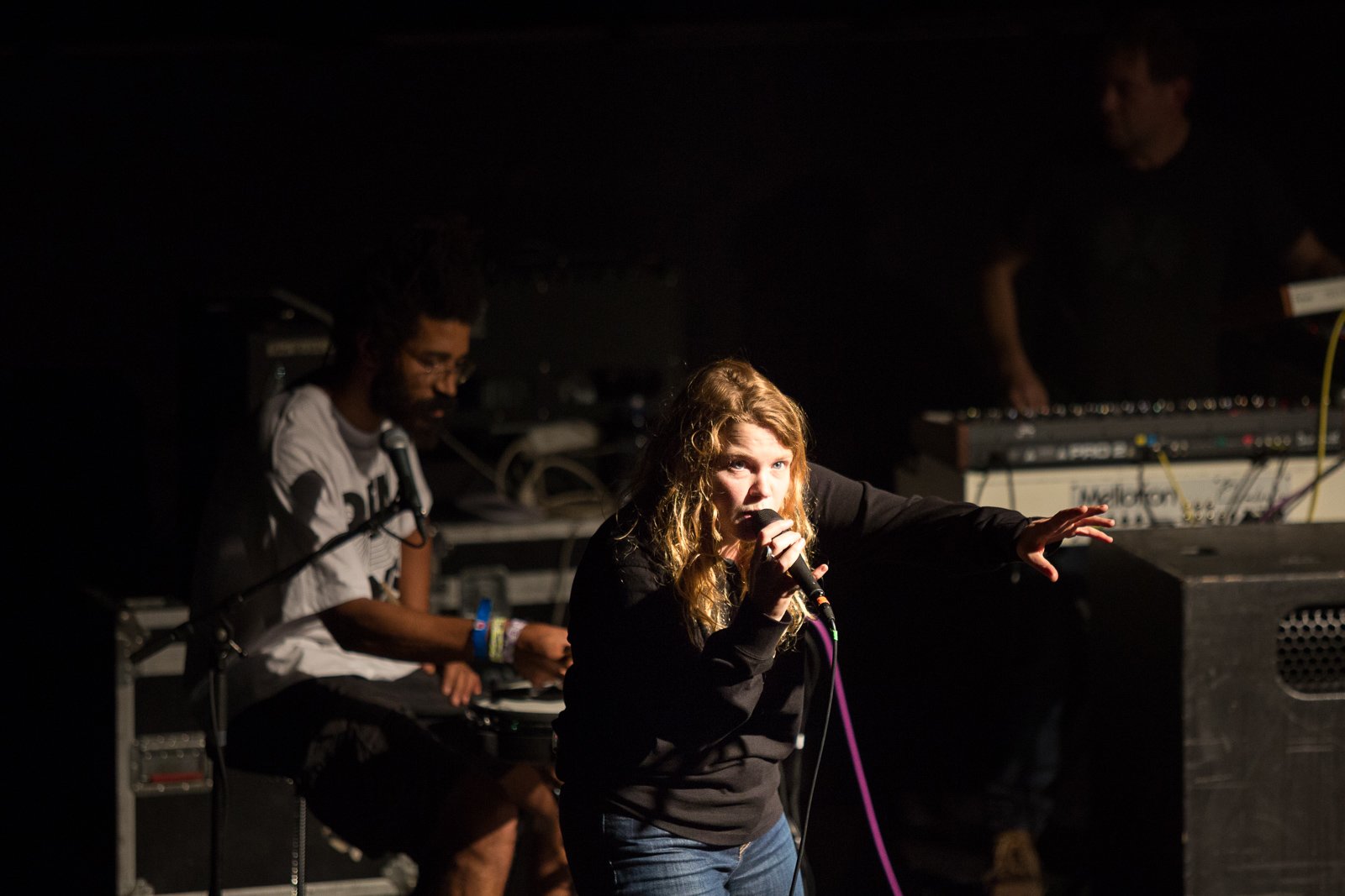 A photograph of Kate Tempest and her drummer performing on stage. She is holding a microphone with her hand outstretched to the crowd. 