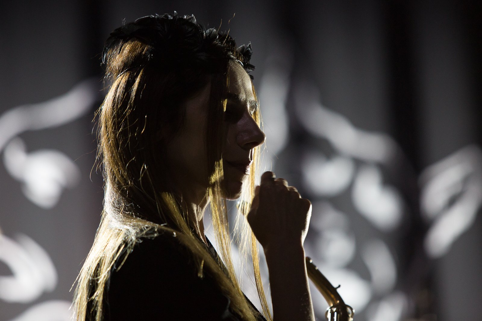 A photo of PJ Harvey holding a microphone, backlit by white light